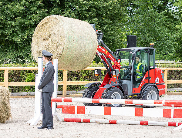 ein Mädchen fährt einen Radlader mit einem Rundballen Heu auf der Gabel