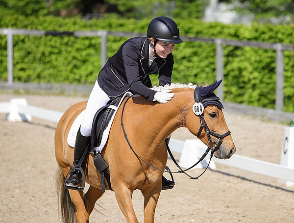 Eine Reiterin klopft ihrem Pony lachend den Hals.