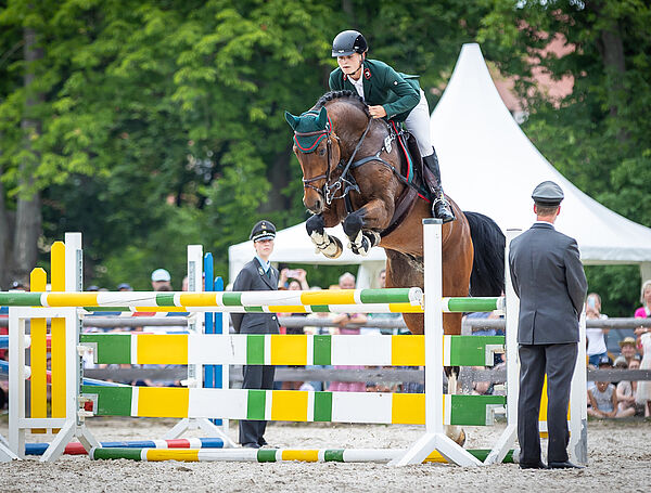 ein braunes Pferd mit Reiterin am Sprung
