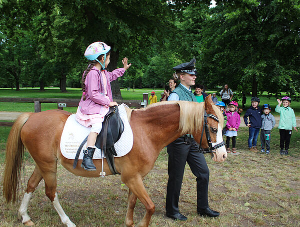 ein Kind sitzt auf einem Pony und winkt den anderen Kindern im Hintergrund